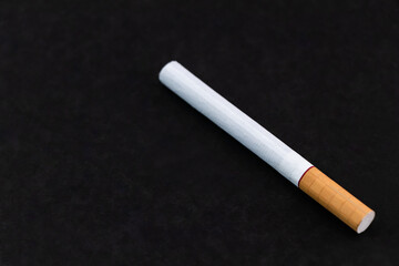 A single cigarette lies on a black surface.