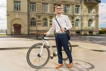 Fototapeta premium A Man in Formal Attire Stands Beside His Bicycle on an Urban Street During a Sunny Afternoon
