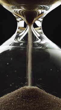 Sand running out in an hourglass, golden sand grains flowing through the glass device, timelapse shot. Time, and urgency concept.