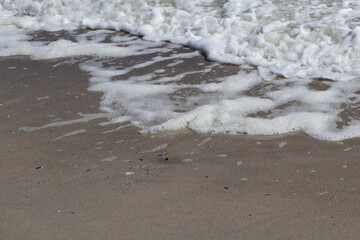 Close-up view of ocean waves gently washing over a sandy beach, leaving a delicate layer of white sea foam on the shore, creating a tranquil and refreshing coastal scene