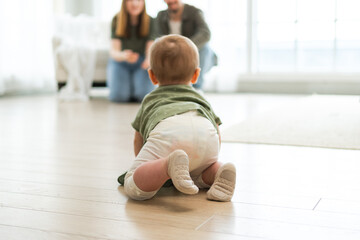 Happy family. Mother father looking at cute little toddler girl crawling on floor in bedroom....