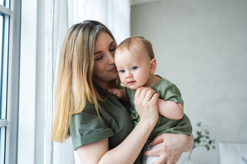 Happy family at home. Mother holding little toddler child daughter. Mom and baby girl relax playing having fun together at home. Mother hugging kissing baby with love care. Mom of breast feeding baby