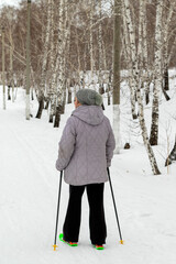 A woman in a grey coat and black pants is standing in the snow with ski poles