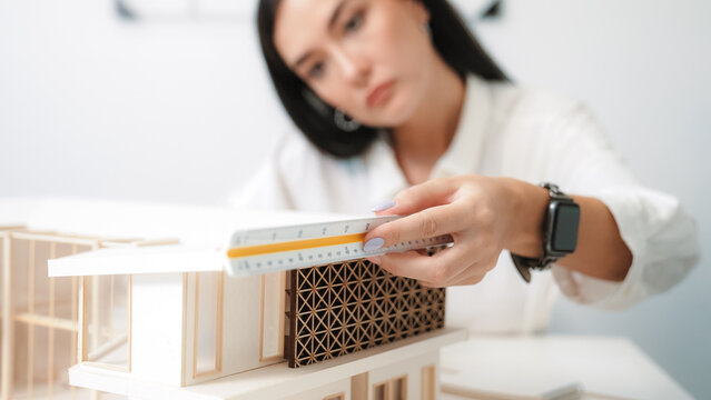 Closeup portrait image of professional young beautiful engineer architect using triangular scale measures house model with focusing at modern office. Business creative design concept. Immaculate.