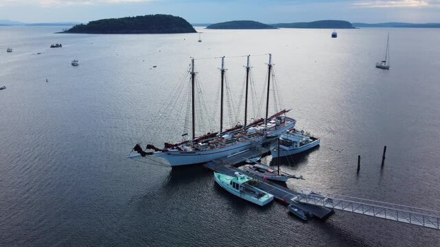 Aerial footage of a four masted schooner moored at the coastline of Bar Harbor at sunset, Maine, USA