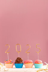 Cupcakes or muffins with buttercream frosting decorated with gold 2025 numbers on pink background....