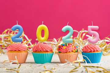 Festive cupcakes and candles in form of numbers 2022 on pink background. Concept of New year.