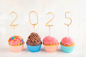 New year cupcakes and gold sparklers numbers 2025. Holiday muffins with pink buttercream frosting on white table