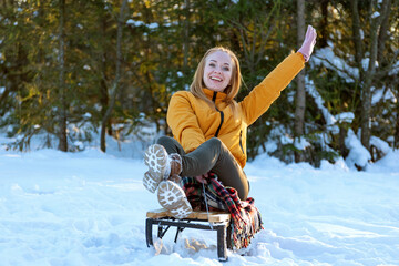 Happy young woman sliding on a sledge in the winter forest.