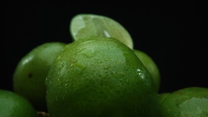 Slices of lime are meticulously arranged in a pile, set against a black background. Each lime slice is captured in stunning detail, its vibrant green hue and enticing texture. Close up. Comestible.