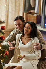 A couple enjoys each others company by the Christmas tree, radiating love and happiness.