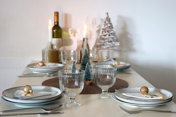 Table set for Christmas meal with plates, glasses, holiday decorations, lit candles and wine. Selective focus.