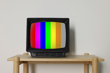 Retro TV set with test pattern on wooden table near white wall. Color bars on screen. No signal