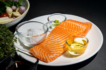 Salmon steak, Raw fillet of sea fish salmon or trout on white dish with salt, oil, and wasabi cream in studio light on dark background.