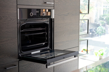 Fototapeta premium Modern minimal Oven building with wooden furniture in Kitchen with full green tree bokeh glass window beside for copy space advertising design.