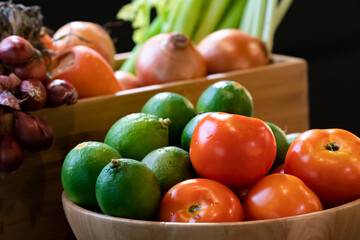 Vegetable tomato and lime in wood bowl with blur background carrot, onion, and red shallot in wood box. All are in studio light.