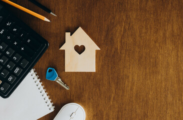 Wooden house model, calculator and key on a wooden table, flat lay.