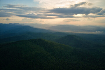 Aerial view of green pine forest with dark spruce trees covering mountain hills at sunset. Nothern woodland scenery from above