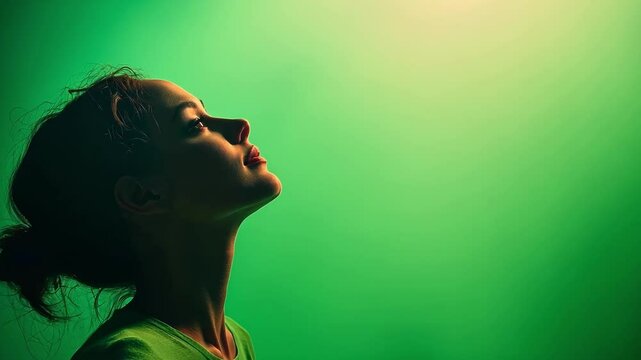 Young woman tilting her head back against a green screen background, showcasing her pulled back hair. The serene pose conveys a sense of tranquility and contemplation