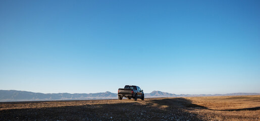 the freedom of exploration, with a solitary vehicle paused on a vast, open landscape, dwarfed by the vastness of the sky and distant mountains on the horizon.