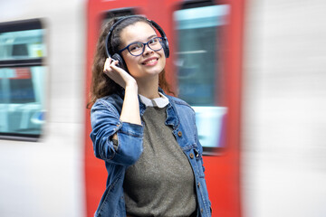 Pretty young girl listening to music with headphones at the train station