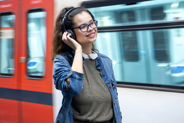 Pretty young girl listening to music with headphones at the train station