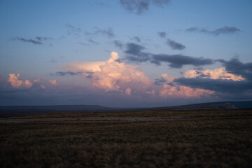 Obraz premium View of a sunset over a field of grass, a beautiful sunset with a purple, pink, and blue as the sun dips below the horizon, dramatic sky at dusk or dawn with fluffy cumulus clouds, mood setting image