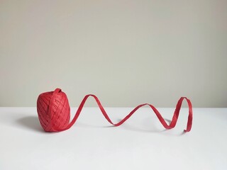 A roll of red raffia ribbon unfurled on a minimalistic background