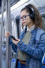 Pretty young girl listening to music with headphones and looks at her phone inside the train