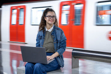 Girl waiting for the train and using her laptop looks at the camera