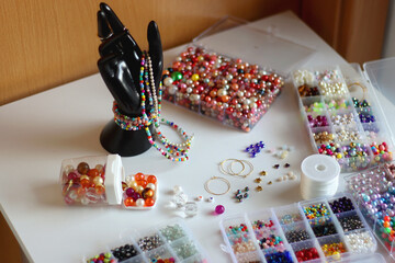 Hand figurine, colorful friendship bracelets, necklaces, various beads and DIY supplies on the table. Making jewelry at home. Selective focus.