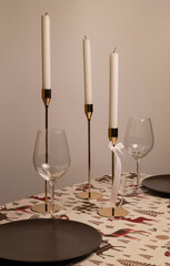The Christmas tablecloth is white with painted red reindeer, and on it stand gold candlesticks with white candles, elegant glass goblets on thin legs, and dark brown ceramic plates.