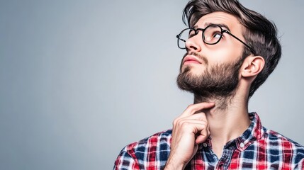 Obraz premium A young man in a plaid shirt and glasses thoughtfully gazes upward, pondering ideas.