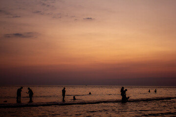 Fototapeta premium a sunset with people standing in the water and one is wearing a pink and orange sunset