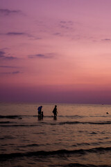 Fototapeta premium a sunset with people standing in the water and one is wearing a pink and orange sunset