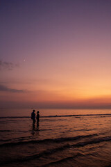 Fototapeta premium a sunset with people standing in the water and one is wearing a pink and orange sunset