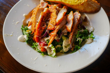 A Caesar salad featuring succulent grilled chicken breast, crunchy croutons made from fresh whole wheat bread with garlic, and an assortment of healthy organic vegetables, drizzled with dressing.