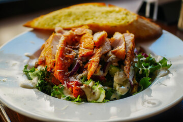 A Caesar salad featuring succulent grilled chicken breast, crunchy croutons made from fresh whole wheat bread with garlic, and an assortment of healthy organic vegetables, drizzled with dressing.