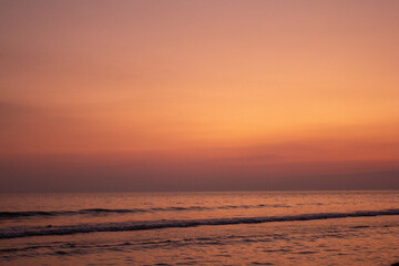 a sunset with people standing in the water and one is wearing a pink and orange sunset