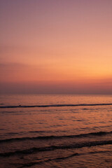 a sunset with people standing in the water and one is wearing a pink and orange sunset