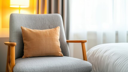 A cozy gray armchair with a decorative golden pillow, softly illuminated by a nearby lamp, set against a bright, airy window.