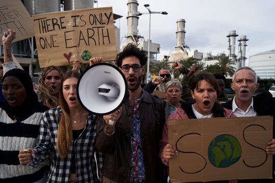Pro-earth demonstration with banners for climate change. Man with megaphone in a protest against pollution. Group of diverse people outdoors manifesting for global warming.