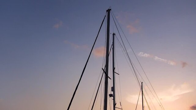 Masts of sailing yachts moored in the port waving in the sky with a reddish sunset. Conceptual.
