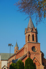 A medieval red brick Gothic-style Catholic church with sharp spires in the center of a quiet little...