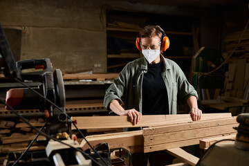 A focused carpenter works diligently with wooden planks in a well-equipped workshop, demonstrating...