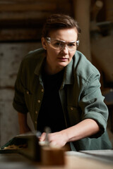 A focused female carpenter engages with wood, demonstrating precision and craftsmanship in her workshop.