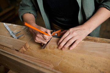 A skilled female carpenter focuses on precision, measuring and marking wood carefully in her...