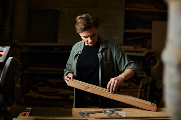 Focused on her task, a female carpenter expertly shapes wood in a workshop brimming with tools and craftsmanship.