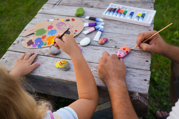 Children education and home school concept. Dad and daughter paint with acrylic paints on sea rocks