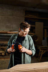 The carpenter prepares her hearing protection while surrounded by wooden materials and tools in her workshop.